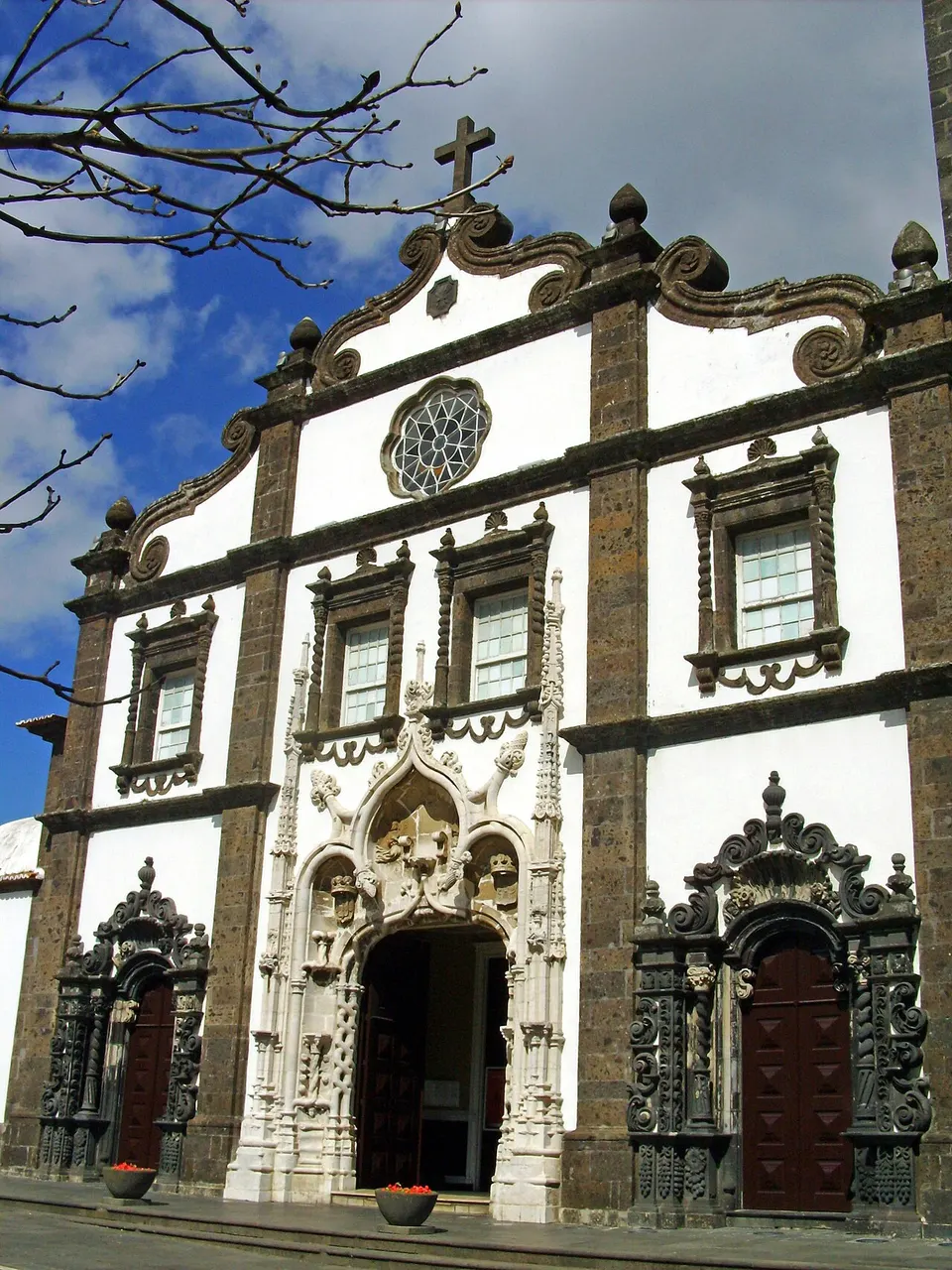 A fachada branca da Igreja de São Sebastião com molduras de basalto escuro, o portal manuelino esculpido e a rosácea.