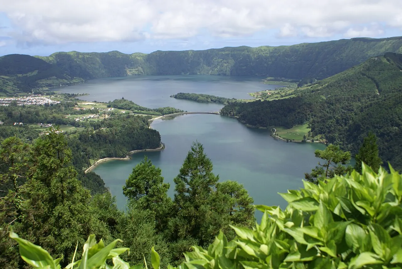 As lagoas Verde e Azul das Sete Cidades vistas do alto do miradouro, com a ponte entre elas, a vila e a cratera em volta.