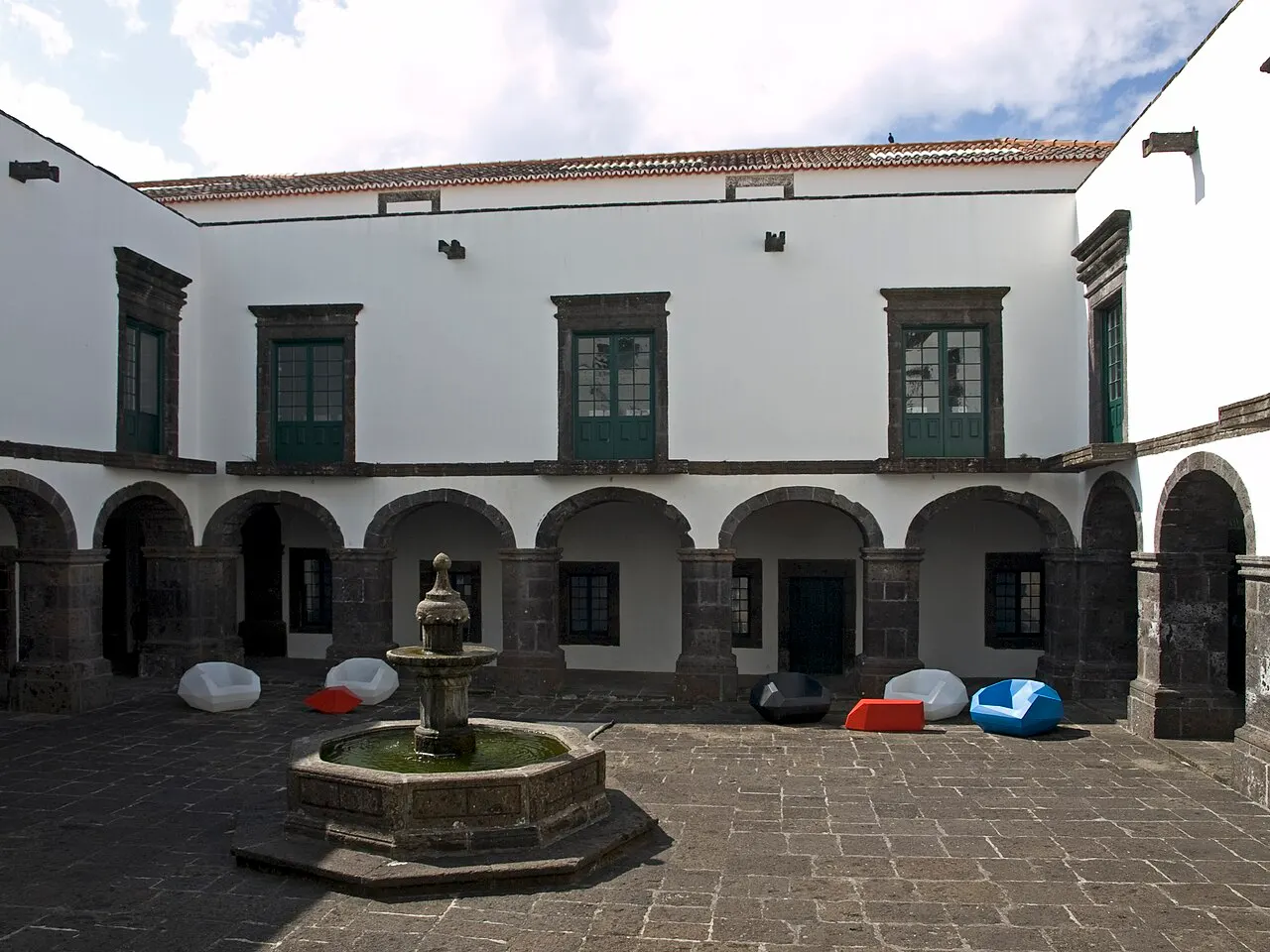 O claustro branco do antigo Convento de Santo André, com arcadas de basalto, janelas verdes e um chafariz no centro do pátio.