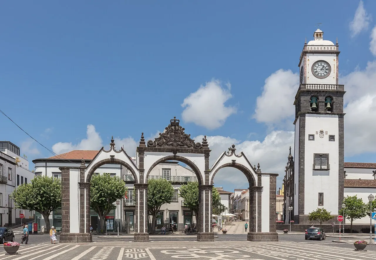 Os três arcos brancos e de pedra escura das Portas da Cidade sobre a calçada desenhada, com a torre branca do relógio ao lado.