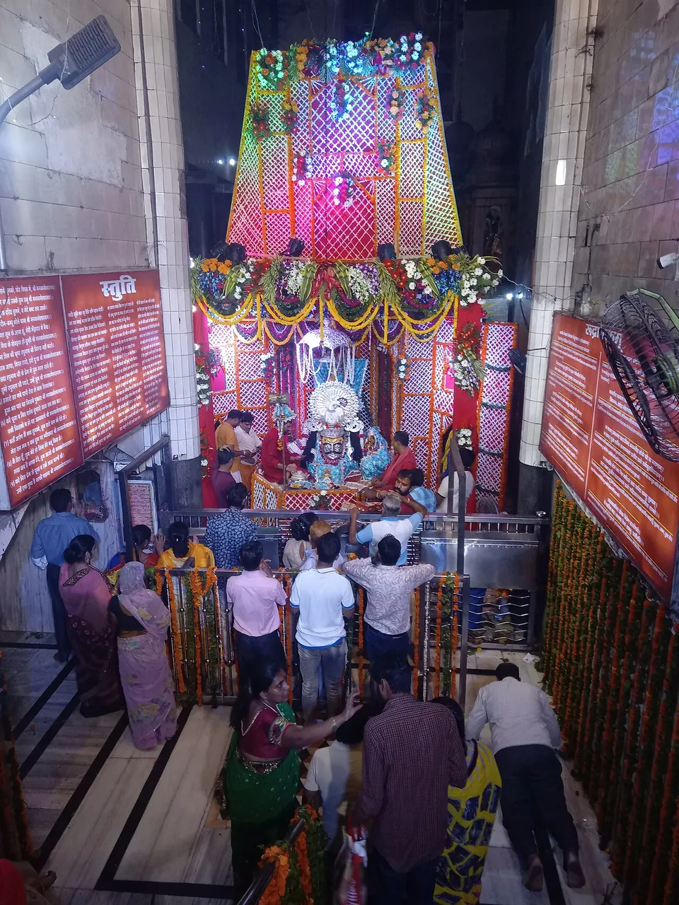 Santuário do templo, com dossel colorido de treliça, pessoas atrás de uma grade e painéis laranja nas paredes.