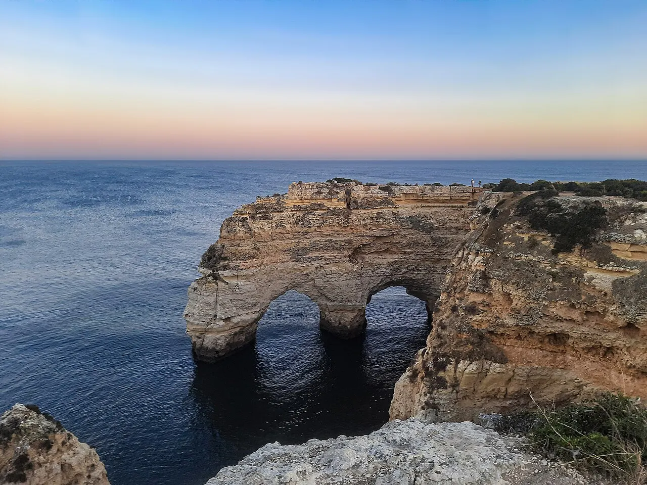 Os arcos de rocha dourada perto da Praia da Marinha, no Percurso dos Sete Vales Suspensos, sobre o mar calmo no fim do dia.