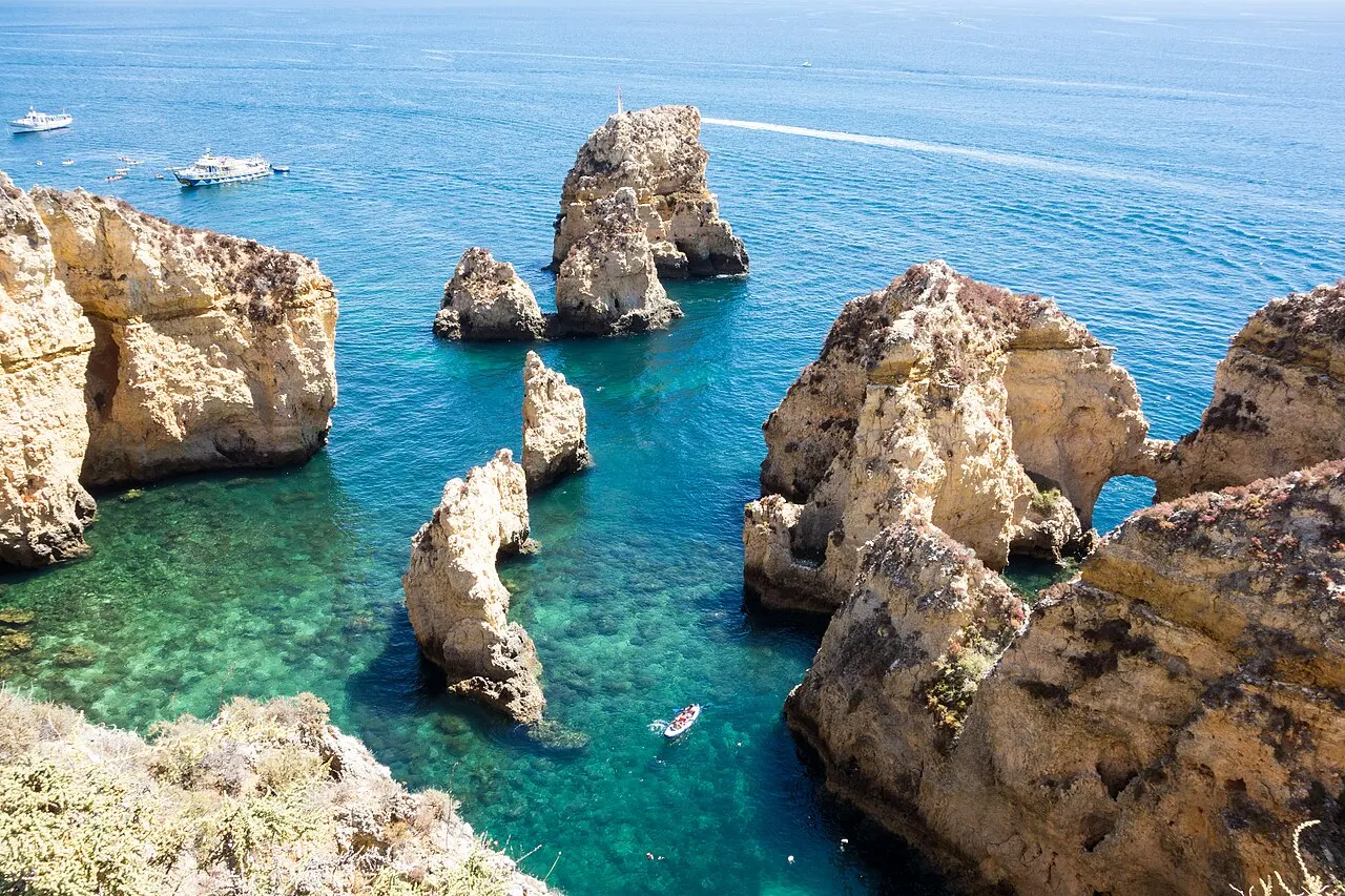 Os rochedos dourados da Ponta da Piedade, em Lagos, vistos do alto, entre a água verde-turquesa e barcos pequenos.