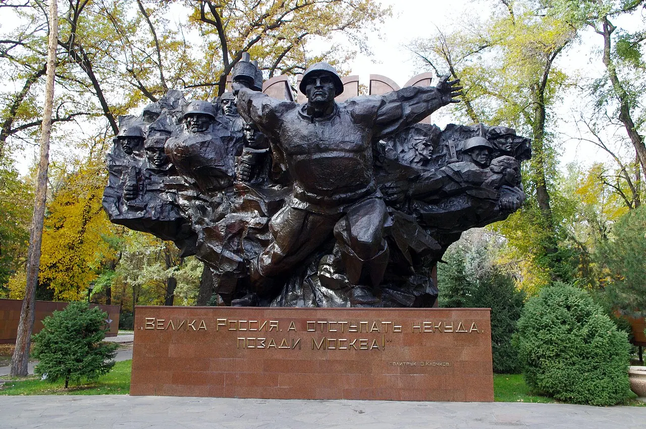 Grande grupo escultórico de bronze escuro com soldados, sobre pedestal de granito vermelho.