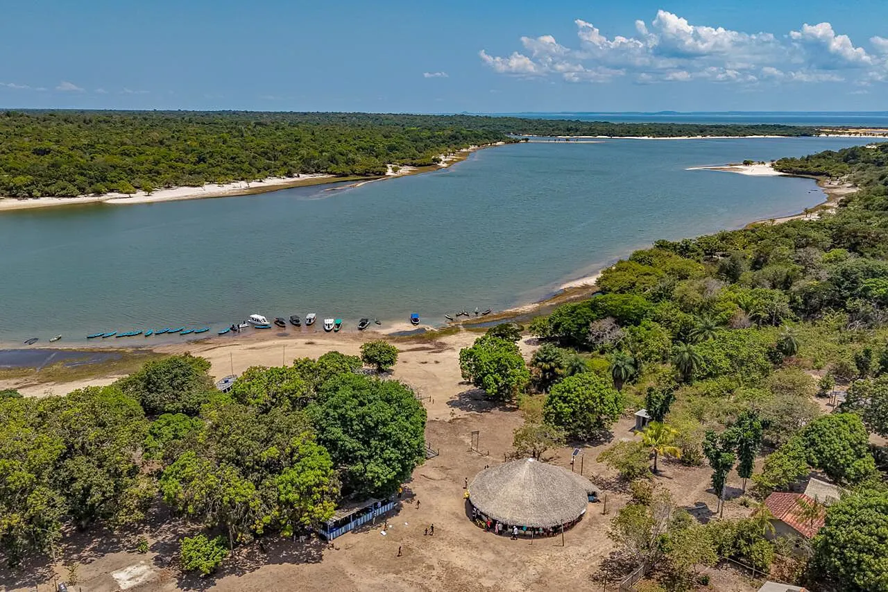 Vista do alto de uma comunidade ribeirinha da Floresta Nacional do Tapajós, com a maloca de palha, a mata e o rio largo ao fundo.