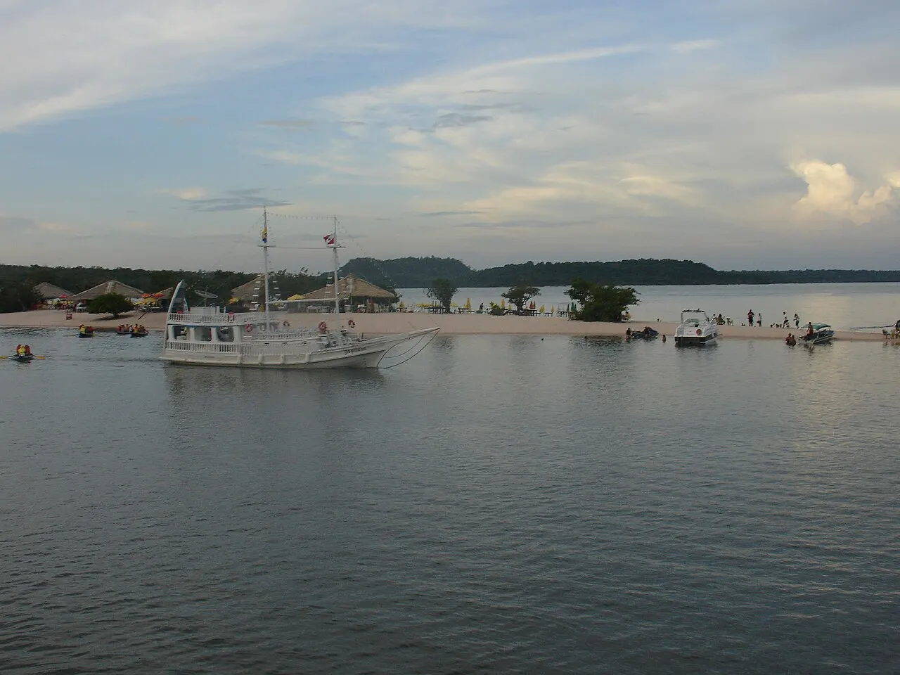 A faixa de areia branca da Ilha do Amor no meio do rio Tapajós, com barcos ancorados na água calma e o céu de fim de tarde.