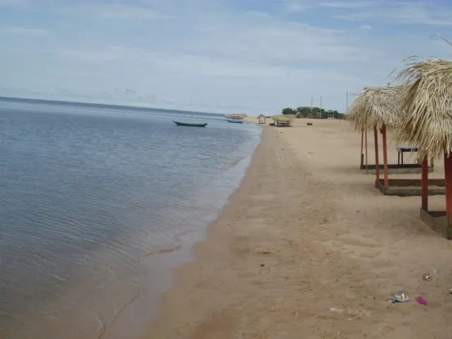 A areia clara da Praia do Pindobal na beira do Tapajós, com barracas de palha e a água calma que se perde no horizonte.