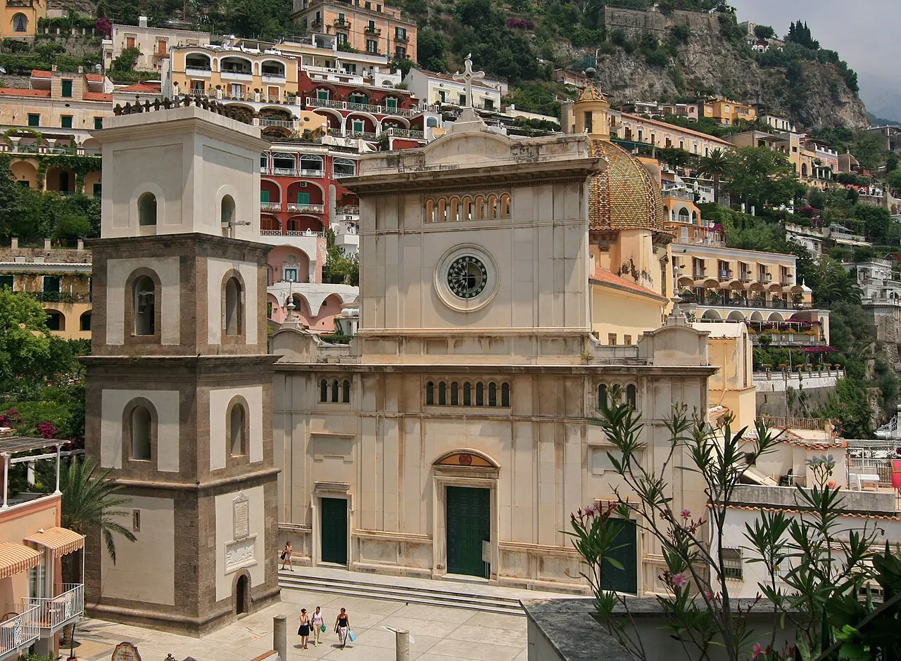 A igreja de Santa Maria Assunta, em Positano, com fachada clara, um campanário quadrado ao lado e as casas coloridas da encosta atrás.