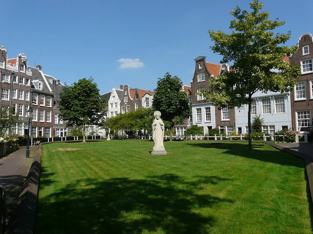 Pátio gramado do Begijnhof, com uma estátua branca no centro e casas de empena ao redor.