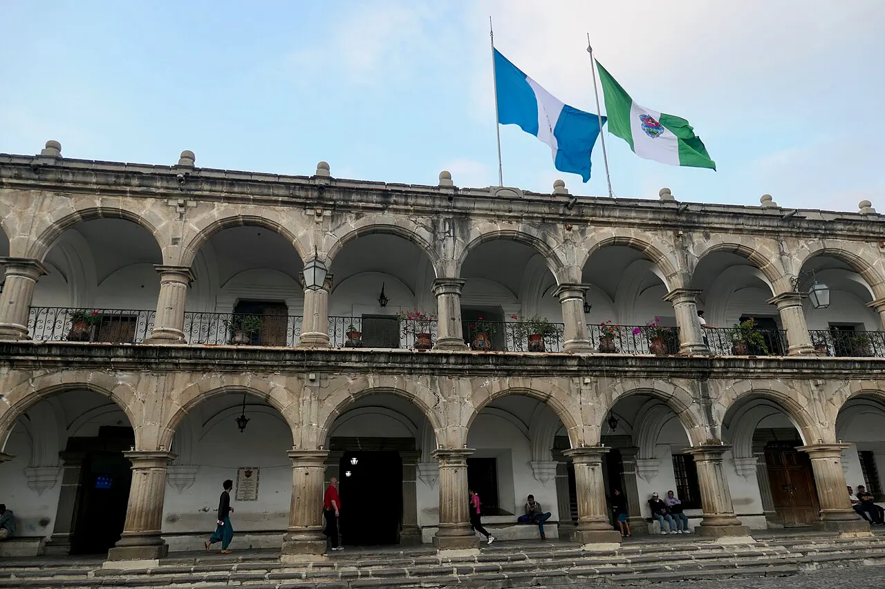 Fachada de dois andares de arcos do palácio, com duas bandeiras no alto e pessoas nos degraus.