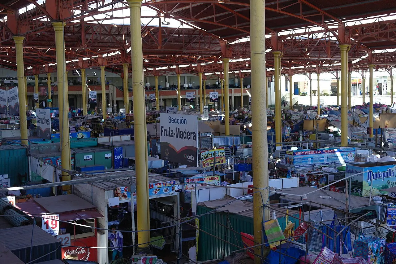 Vista do alto de um grande salão coberto por estrutura de ferro vermelha sobre colunas amarelas, com bancas e placas de seção.