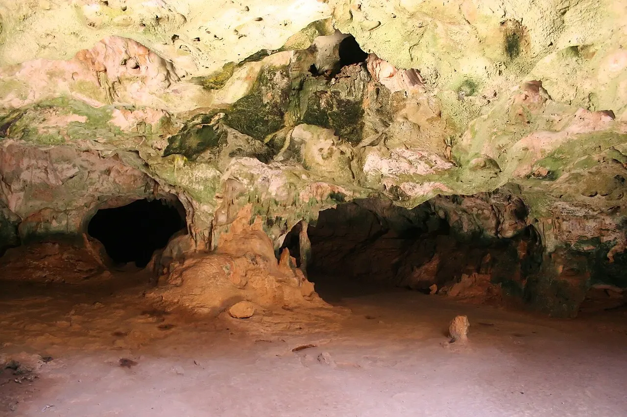 O interior da Guadirikiri Cave, com o teto de calcário manchado de verde e duas aberturas escuras para câmaras mais adiante.