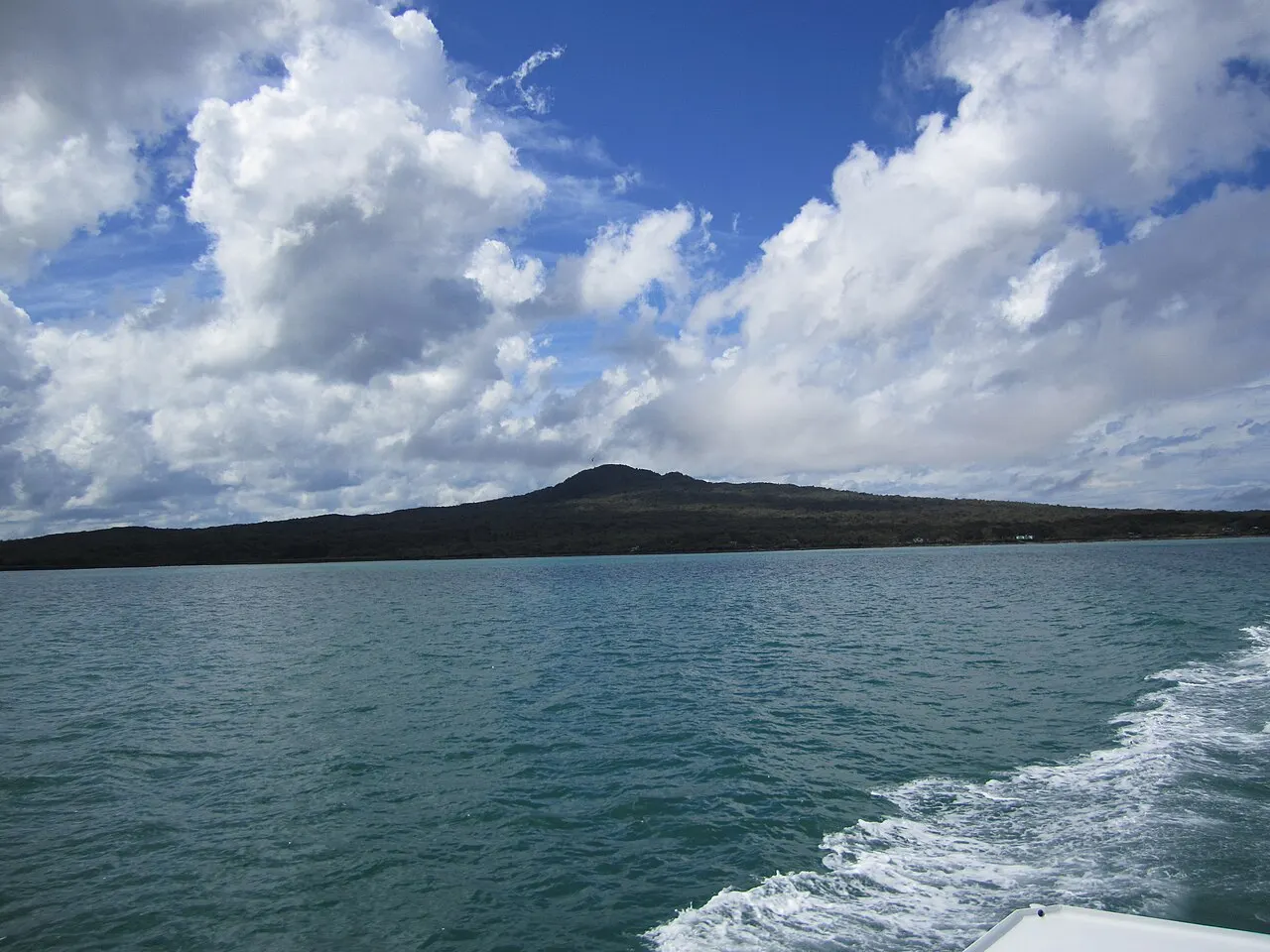 Cone da ilha de Rangitoto visto do mar, com a esteira de um barco no primeiro plano.