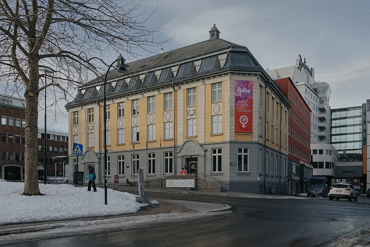 Fachada sul do Nordnorsk Kunstmuseum, em Tromsø, um prédio de esquina de pedra clara com banners.