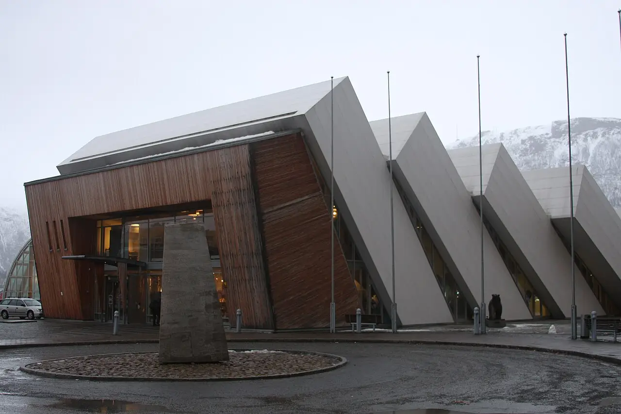 Fachada do Polaria, com telhados inclinados de madeira e concreto, mastros e uma montanha nevada atrás.