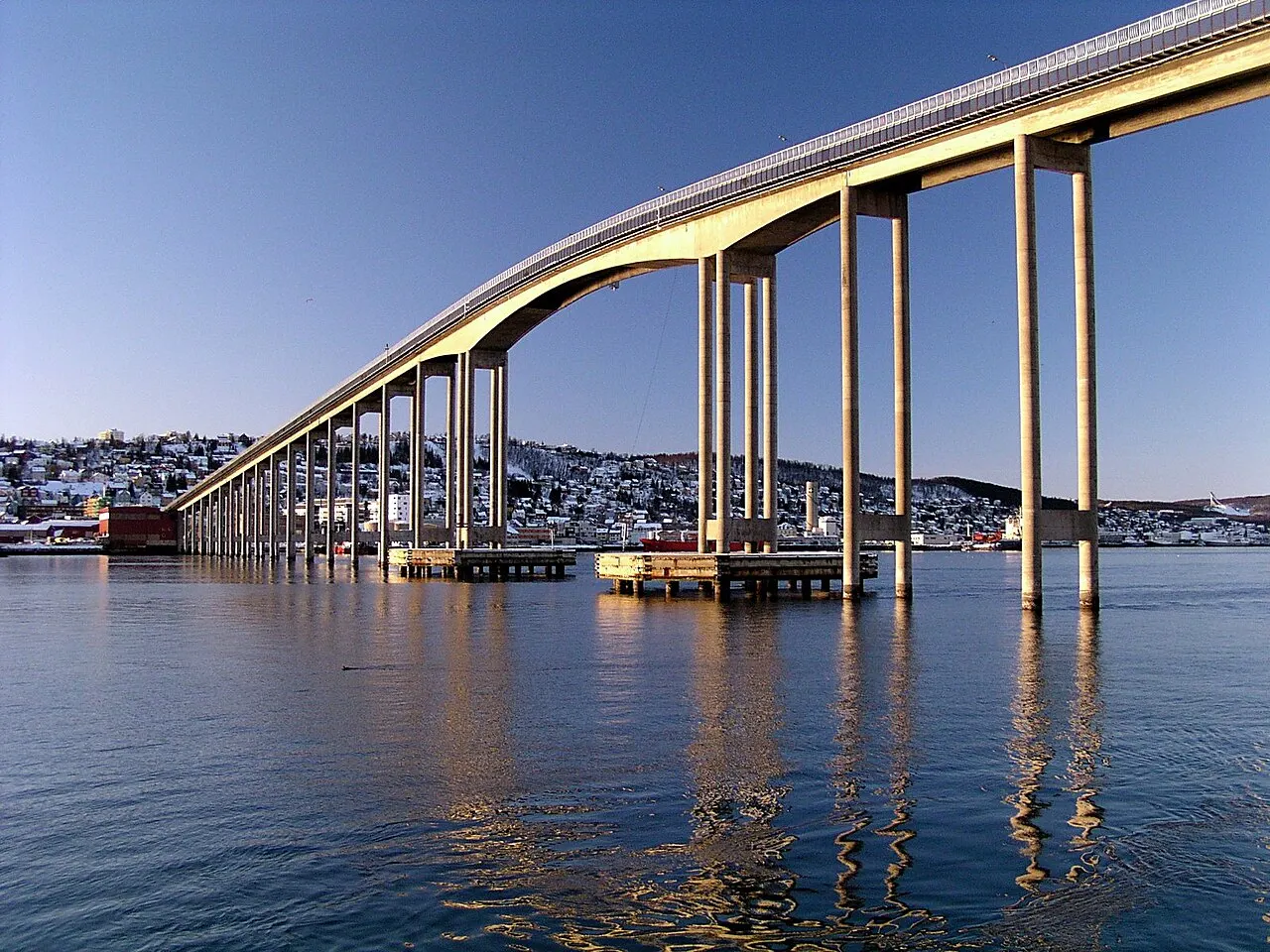 Ponte de concreto sobre a água, com a cidade na encosta ao fundo.