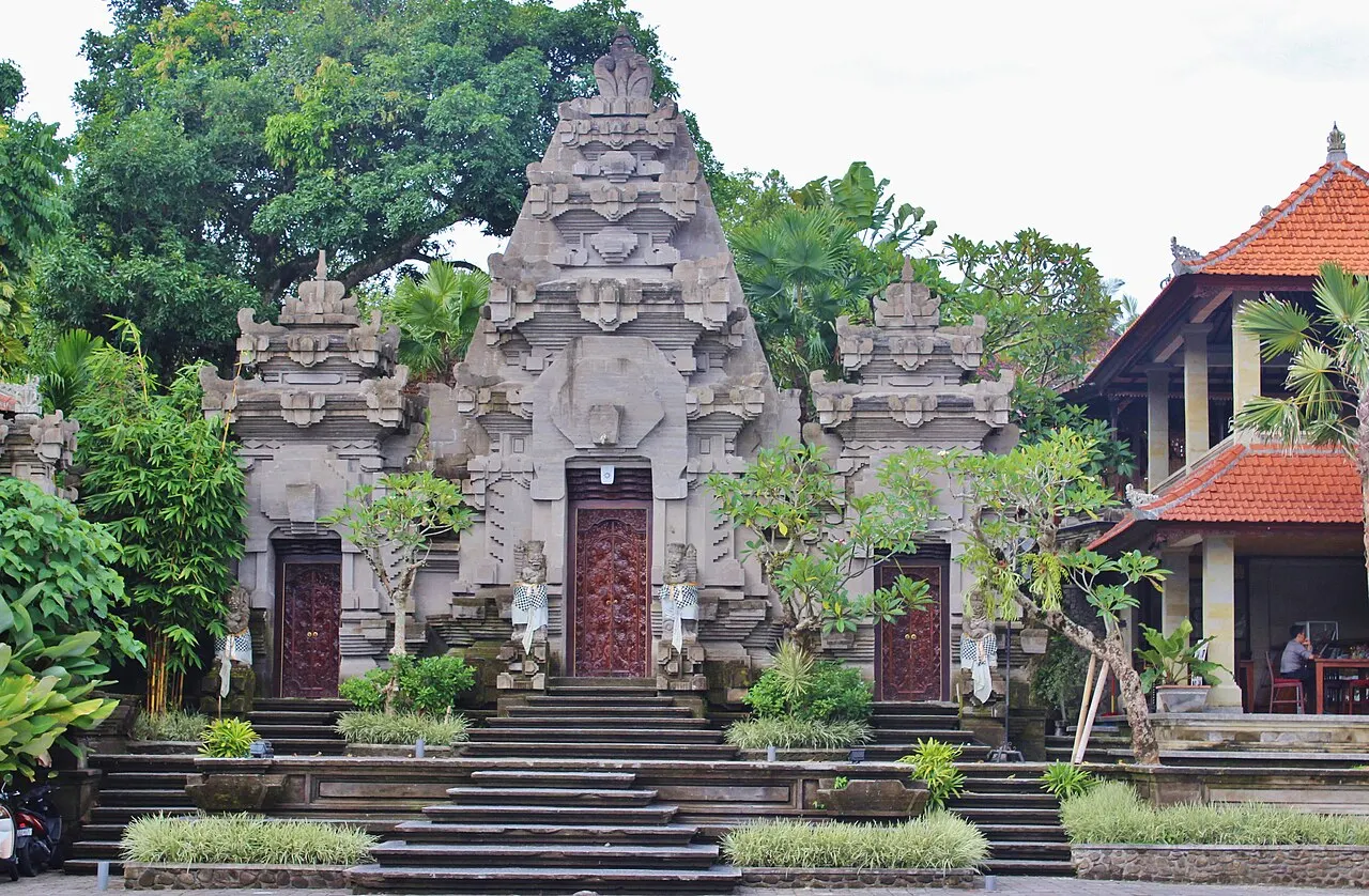 Portão de pedra cinza esculpida, com duas portas vermelhas e plantas crescendo entre as pedras.
