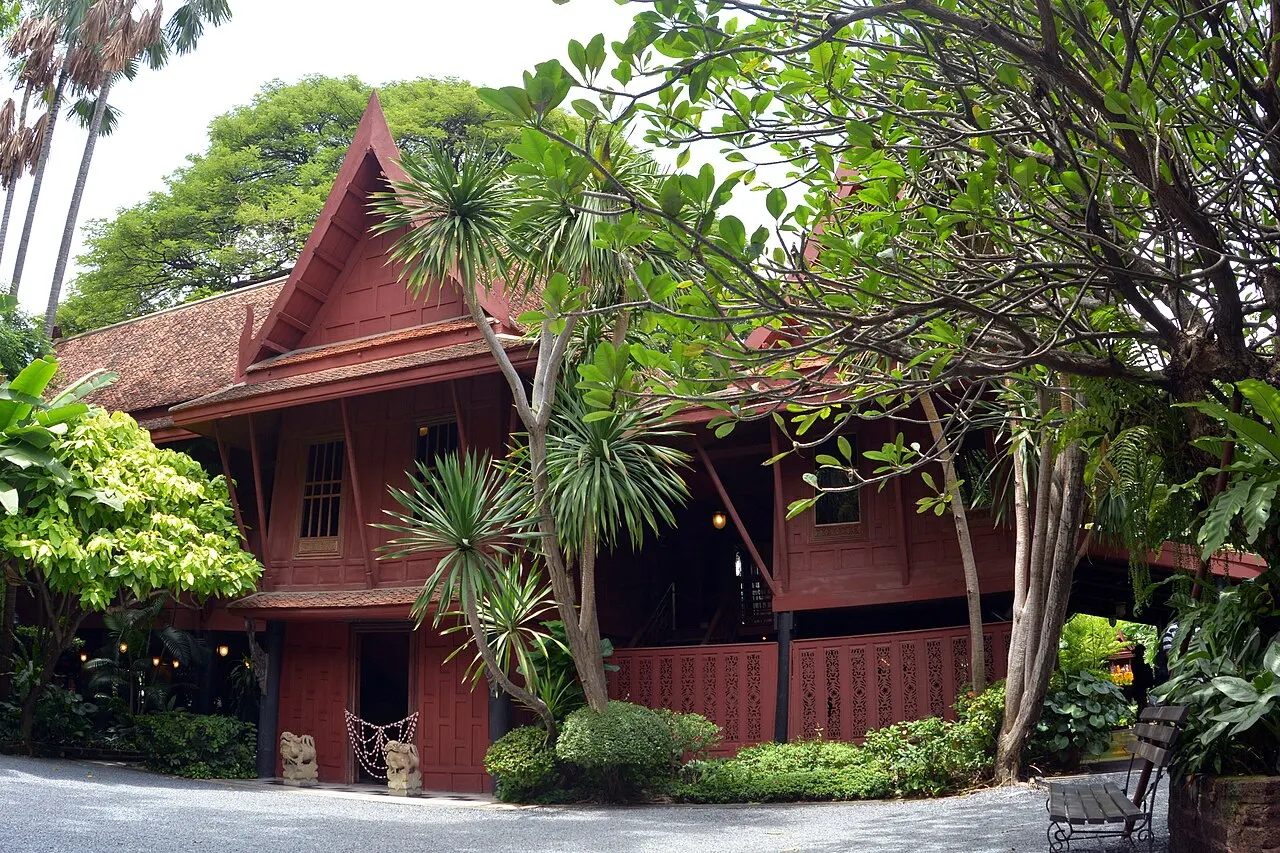 Casa de madeira vermelha de telhado alto, entre as árvores do jardim.