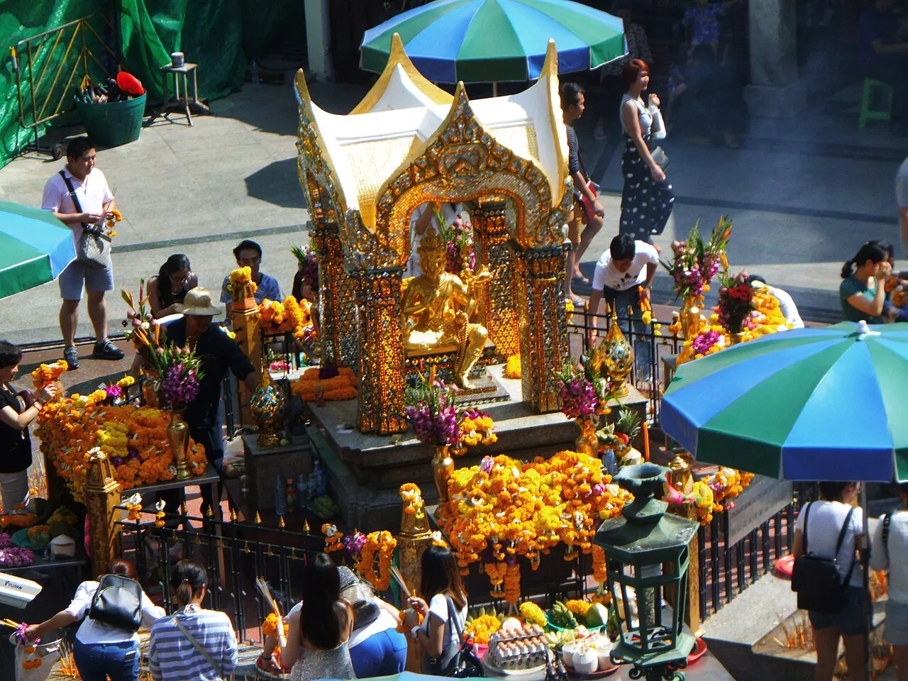 Pequeno pavilhão dourado de telhado pontudo, com uma estátua e flores nas oferendas.