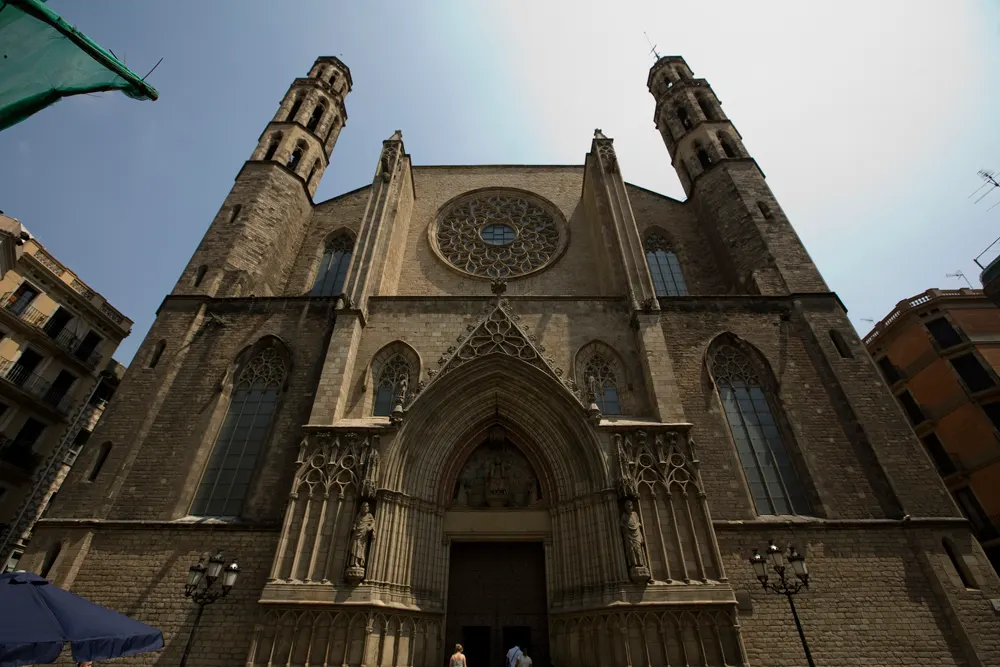 Fachada gótica da igreja Santa Maria del Mar vista de baixo, com duas torres octogonais, um rosáceo central e o portal esculpido sob um céu claro.