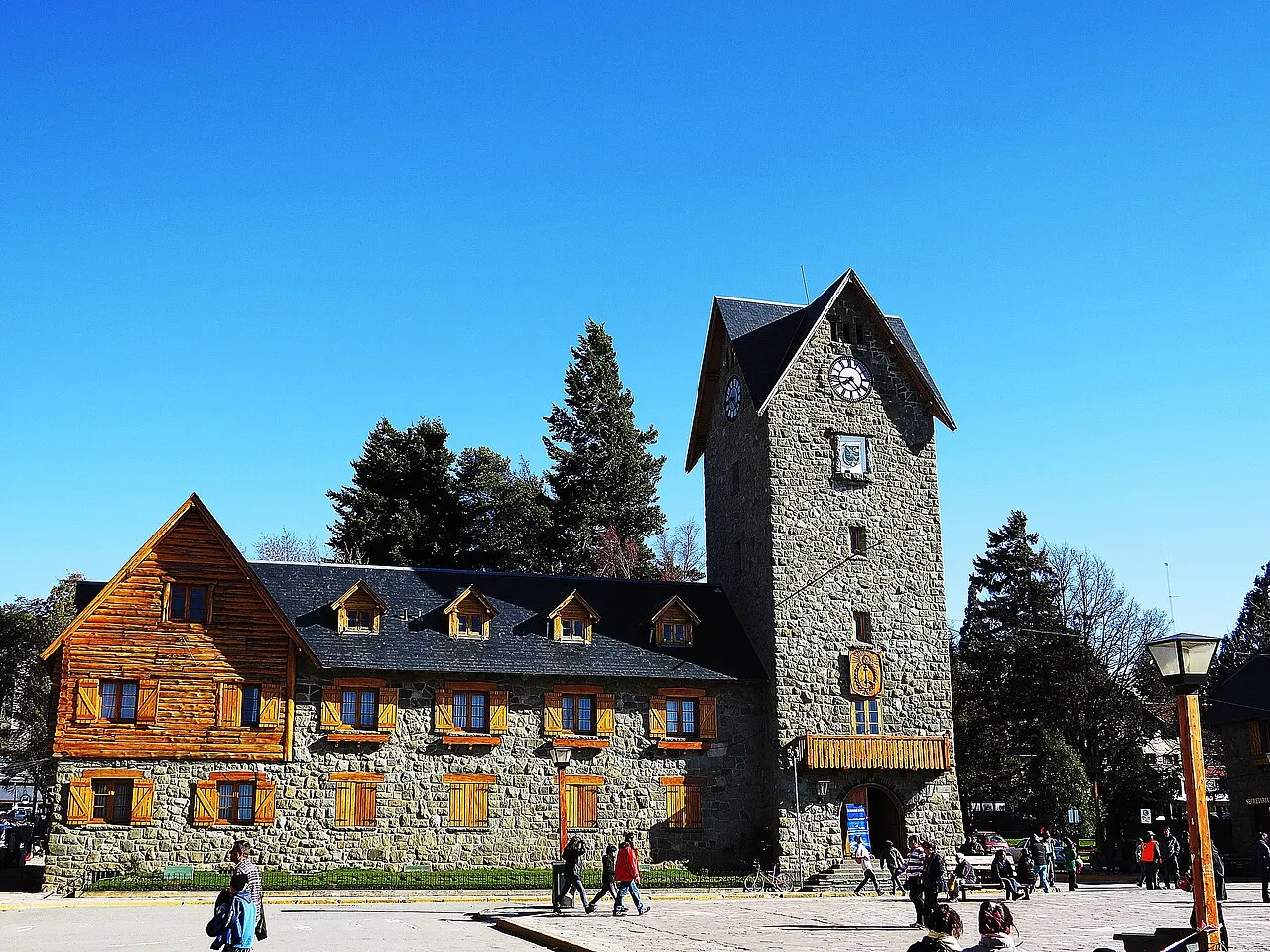 Prédio de pedra e madeira da Municipalidade no Centro Cívico de Bariloche, com a torre do relógio, sob céu azul.