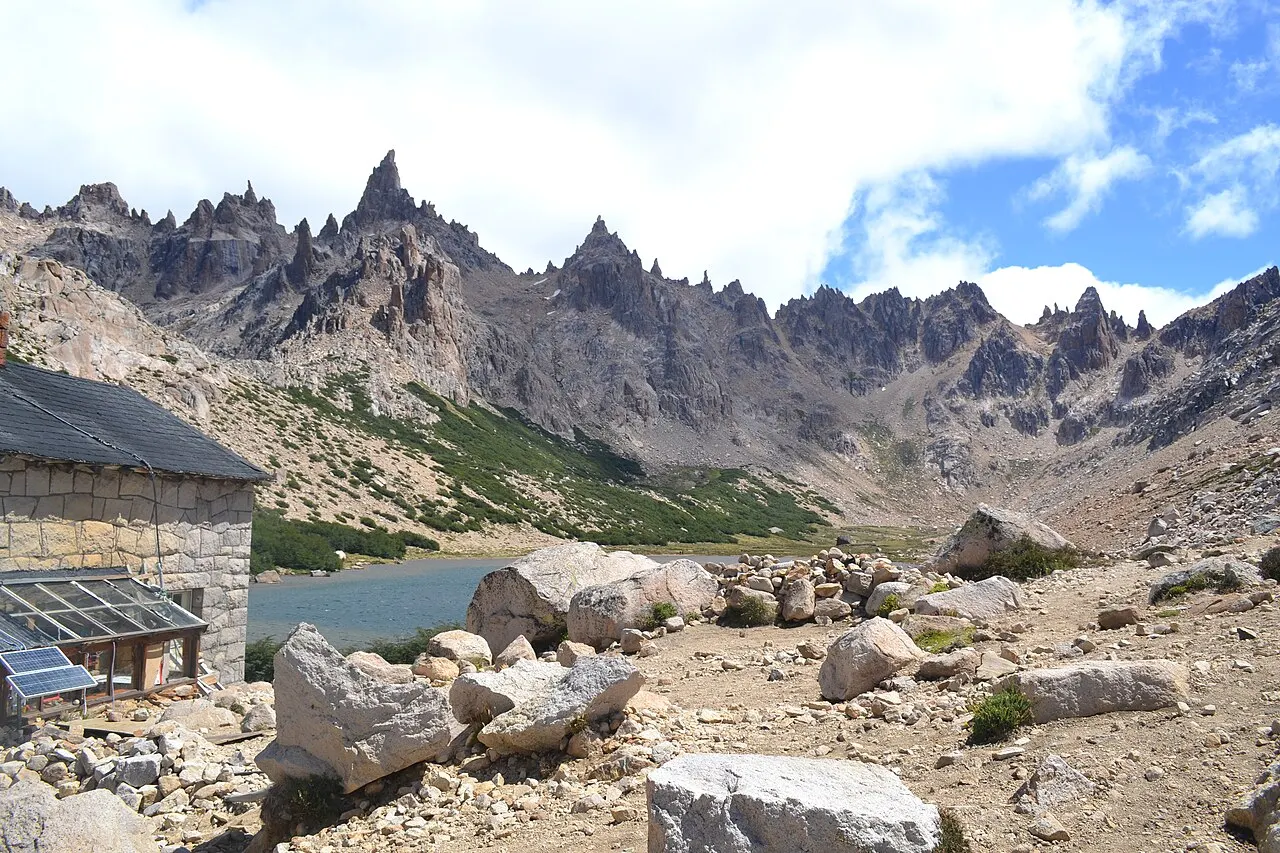 Agulhas de rocha do Cerro Catedral, com um lago e uma casa de pedra na encosta.