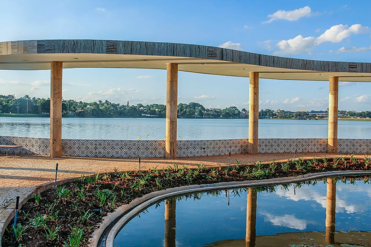 A marquise curva da Casa do Baile apoiada em colunas finas, refletida no espelho d'água, com a lagoa ao fundo.