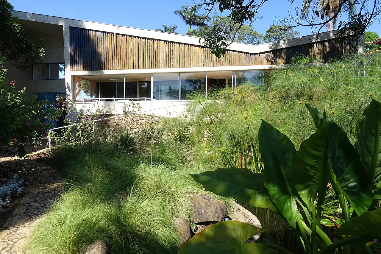 A casa modernista do Museu Casa Kubitschek vista do jardim tropical, com plantas altas em primeiro plano.