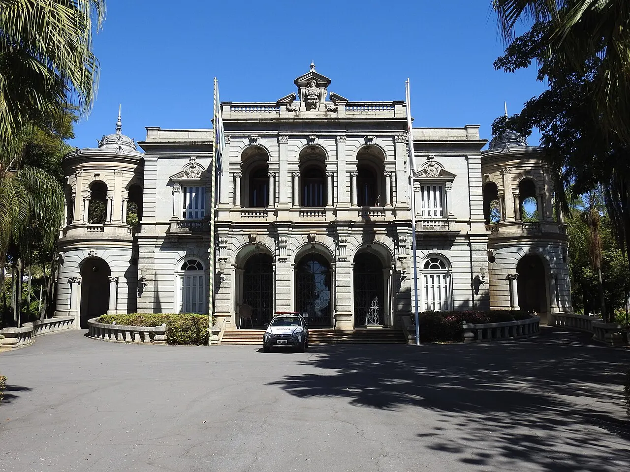 A fachada eclética e cinza do Palácio da Liberdade, com arcos e balcões, vista do pátio sob céu azul.