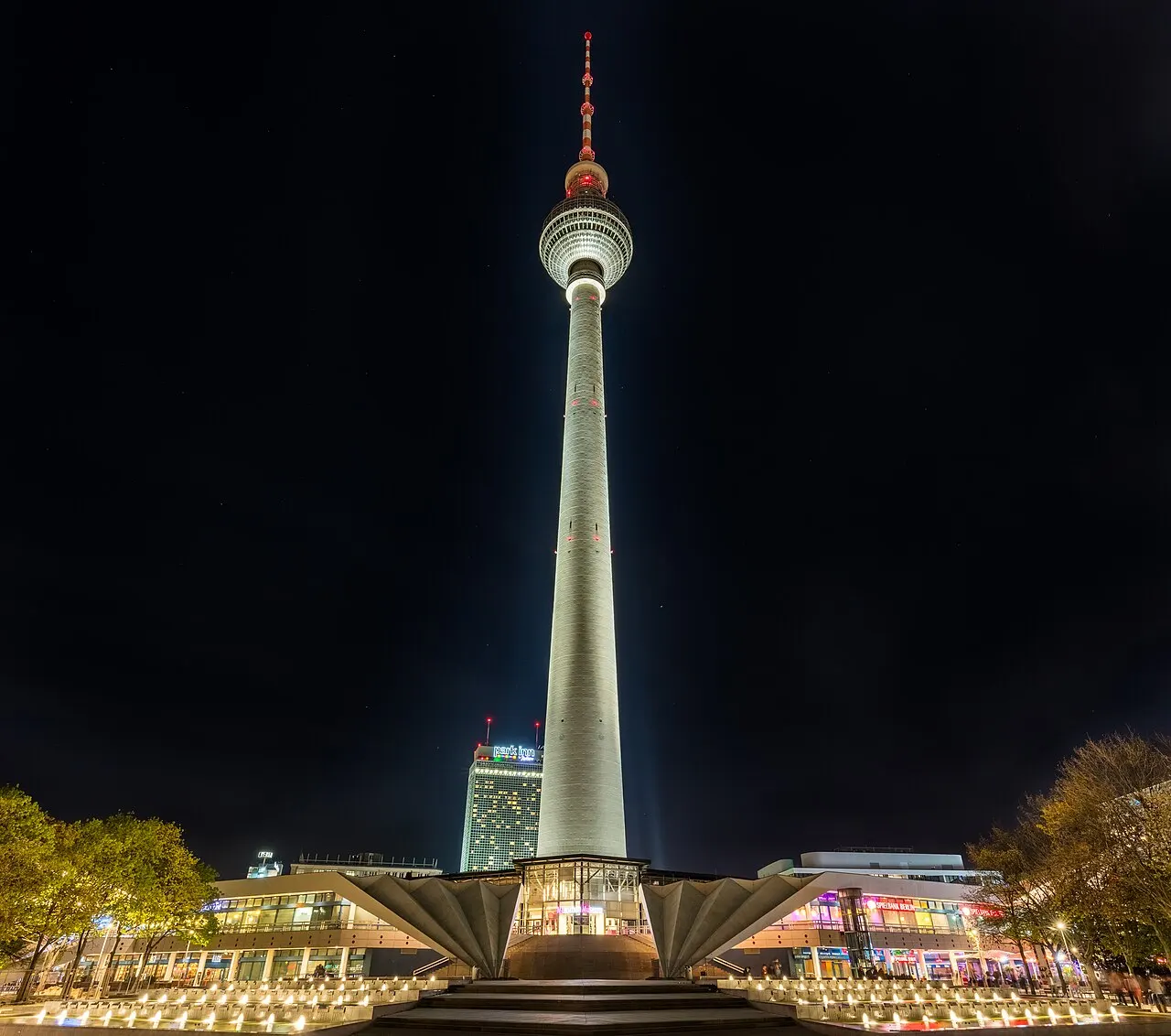 Torre de TV de Berlim, na Alexanderplatz, iluminada à noite, com a esfera perto do topo.