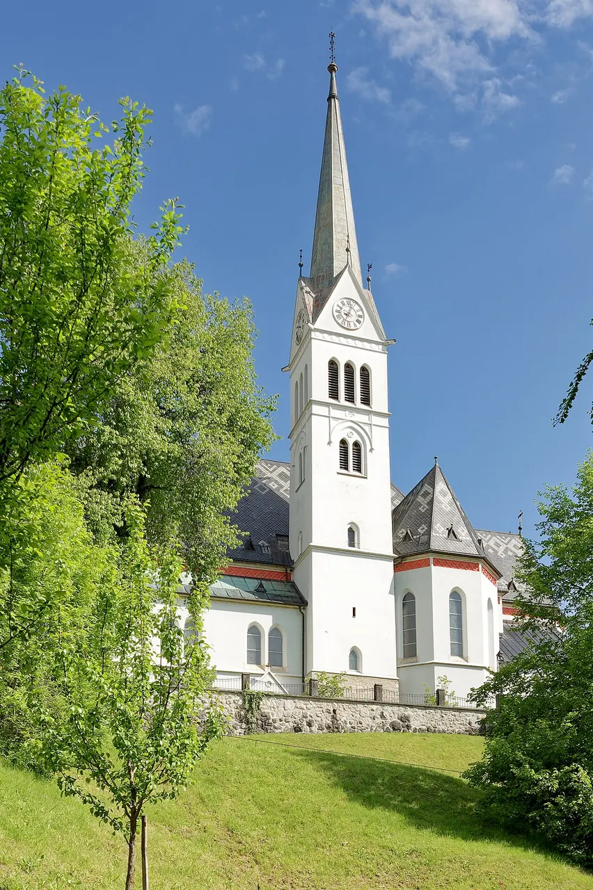 A Igreja paroquial de São Martinho, branca, com a torre alta e pontuda, entre árvores e gramado sob céu azul.