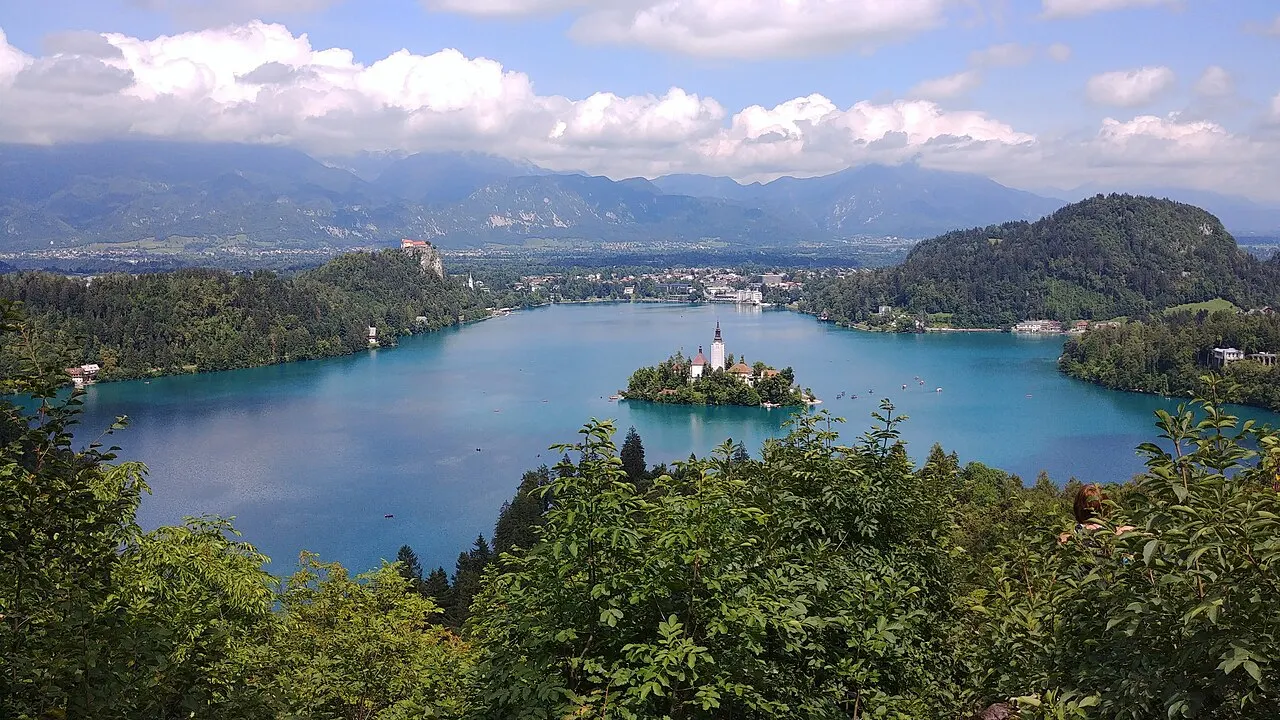 O Lago de Bled e a ilha vistos do mirante de Ojstrica, com o castelo à esquerda e as montanhas no horizonte.