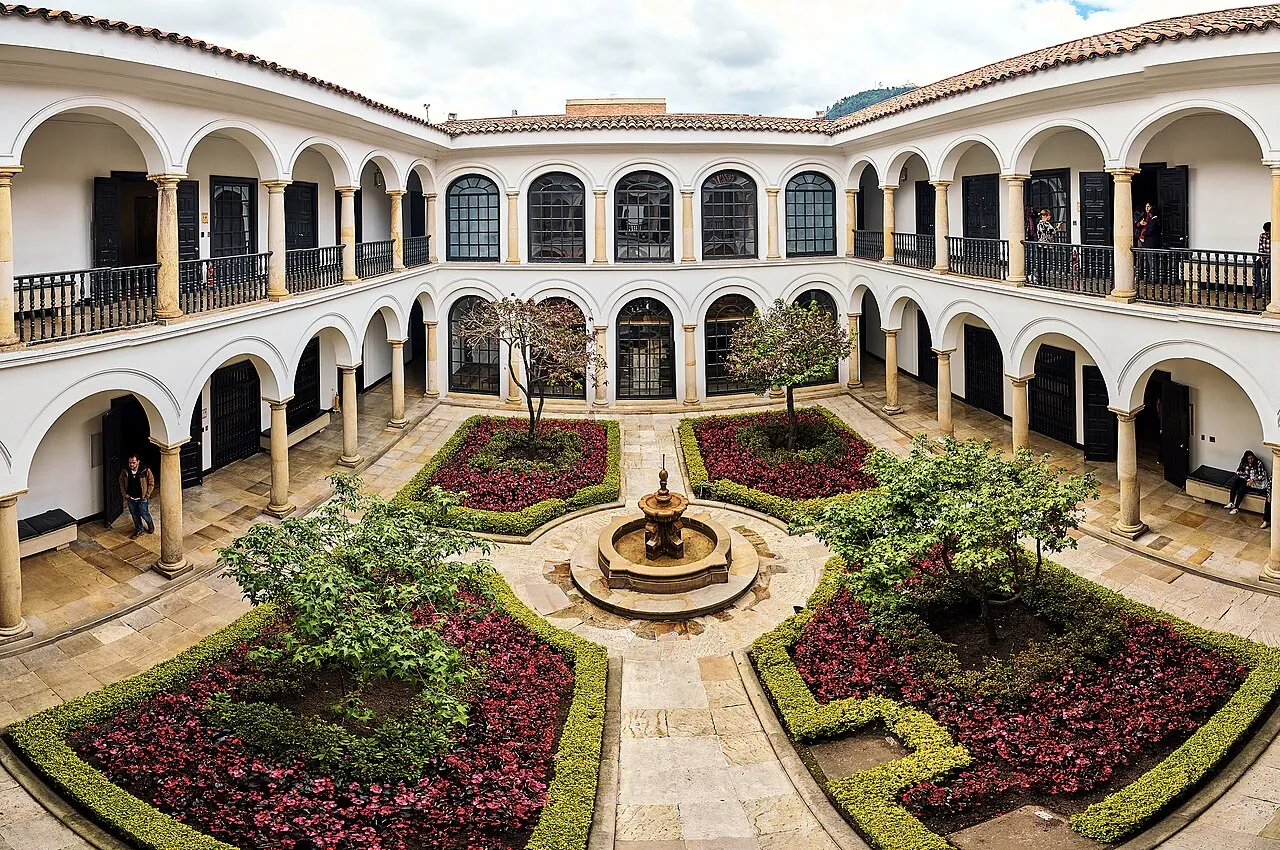 Pátio do museu, com arcos brancos, uma fonte no centro e canteiros vermelhos.