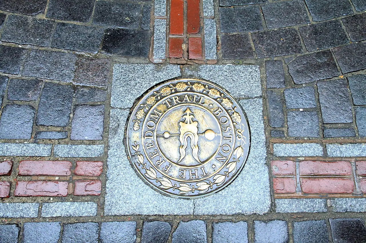 Un medallón de bronce del Freedom Trail incrustado en el pavimento de Boston, entre ladrillos rojos.