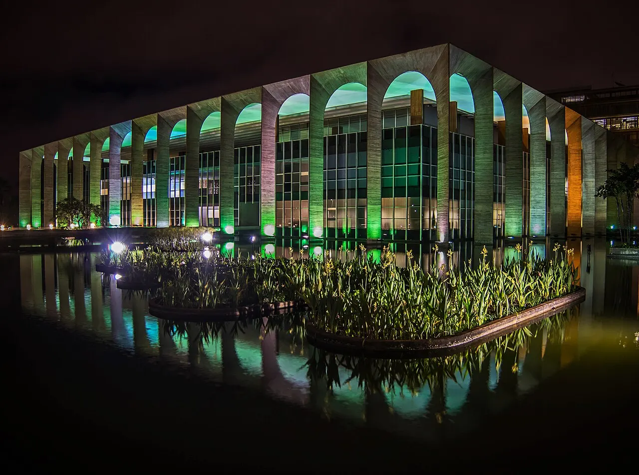 Palácio do Itamaraty, em Brasília, com os arcos de concreto iluminados e o espelho d'água à frente.