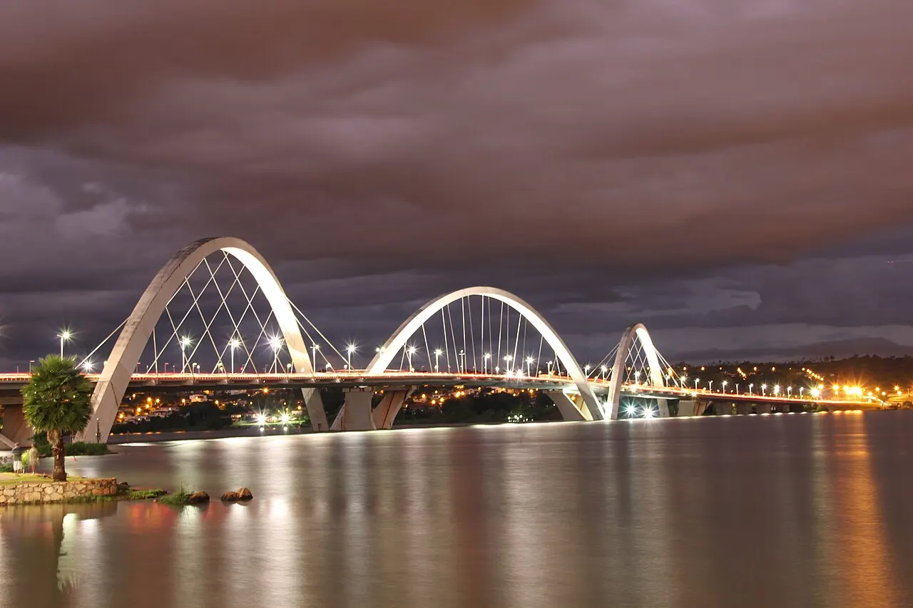 Ponte Juscelino Kubitschek, em Brasília, com os três arcos cruzados sobre o lago Paranoá, à noite.