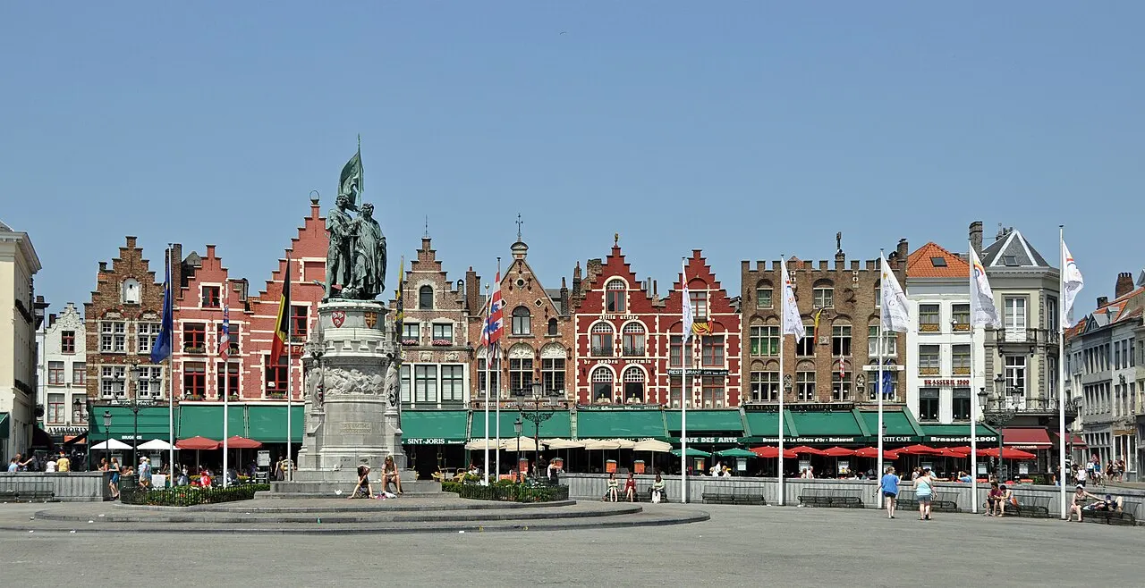 O lado norte do Markt, com fachadas coloridas de empena escalonada, toldos verdes e a estátua de Jan Breydel e Pieter de Coninck no centro.