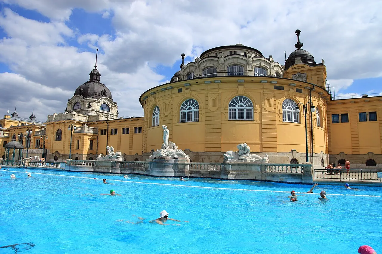 Prédio amarelo dos Banhos Széchenyi, em Budapeste, com cúpulas, visto da piscina ao ar livre.