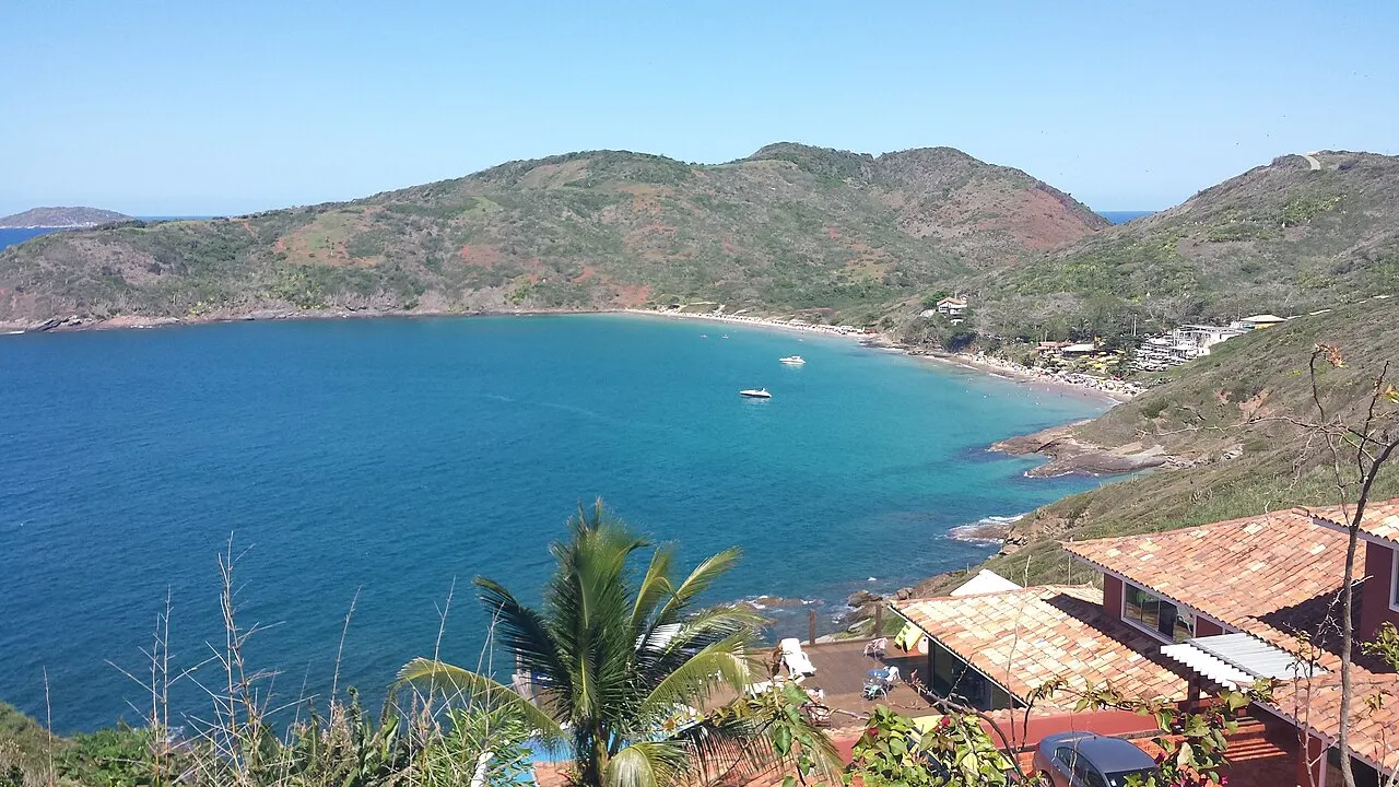 A curva da Praia Brava vista do alto, com o mar azul aberto e os morros cobertos de vegetação.