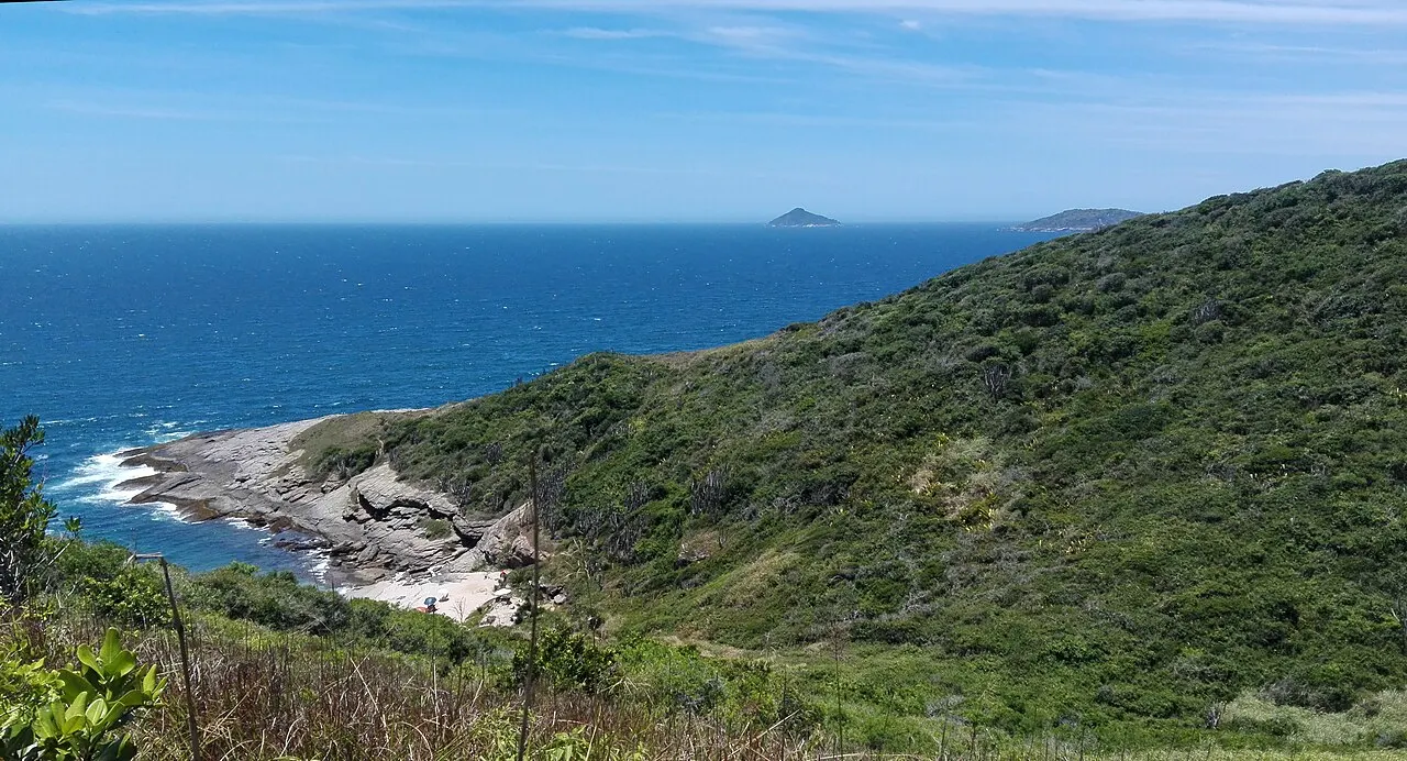 The rocky, scrubby coast around Olho de Boi, with the open blue sea and an island on the horizon.