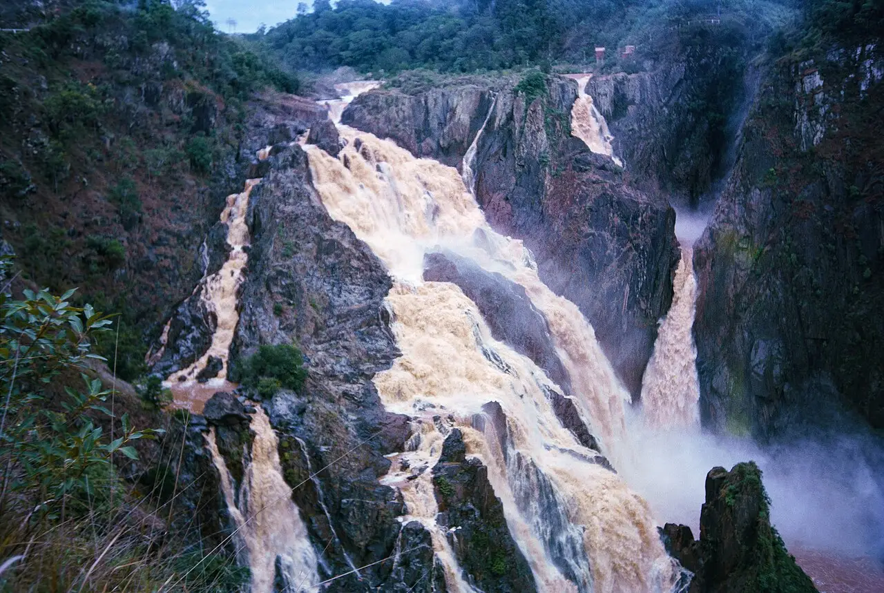 Barron Falls, cachoeira de água barrenta em vários braços, no desfiladeiro de rocha, com mata nas bordas.