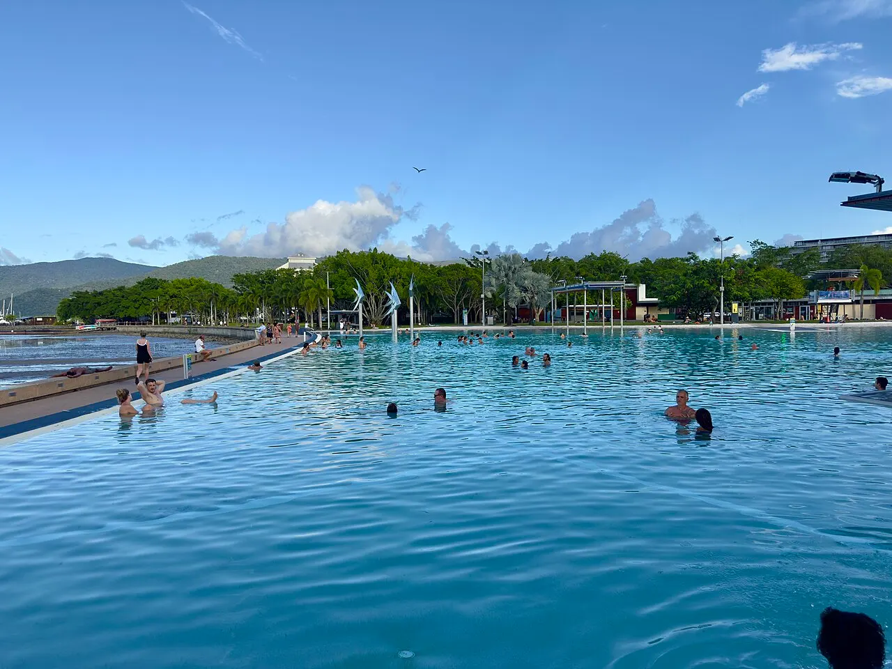A piscina da Esplanade Lagoon ocupa o quadro, com gente na água, a passarela à esquerda e morros ao fundo.