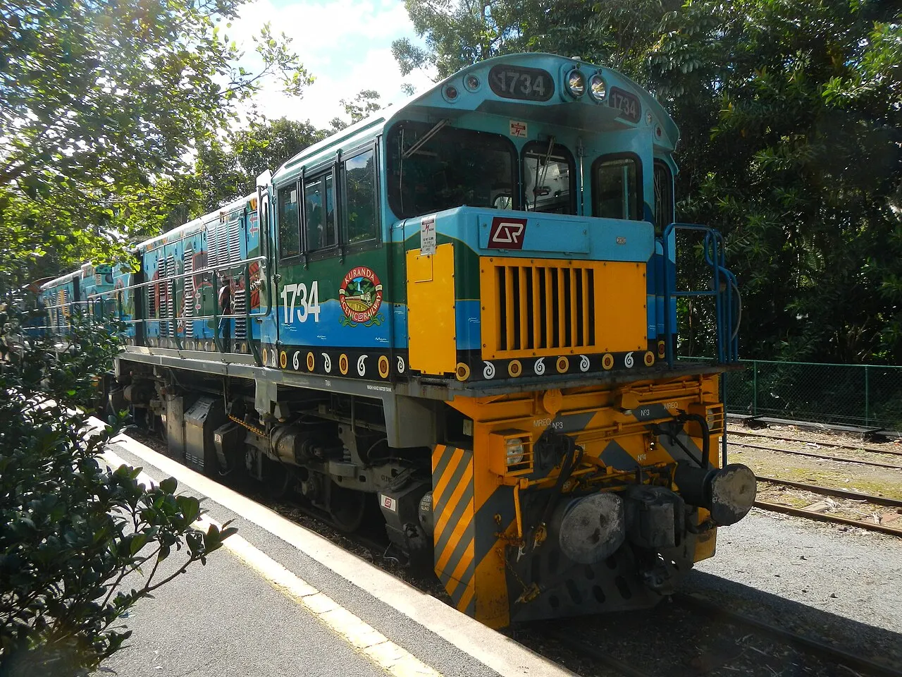 A composição do Kuranda Scenic Railway parada na plataforma, entre as árvores.