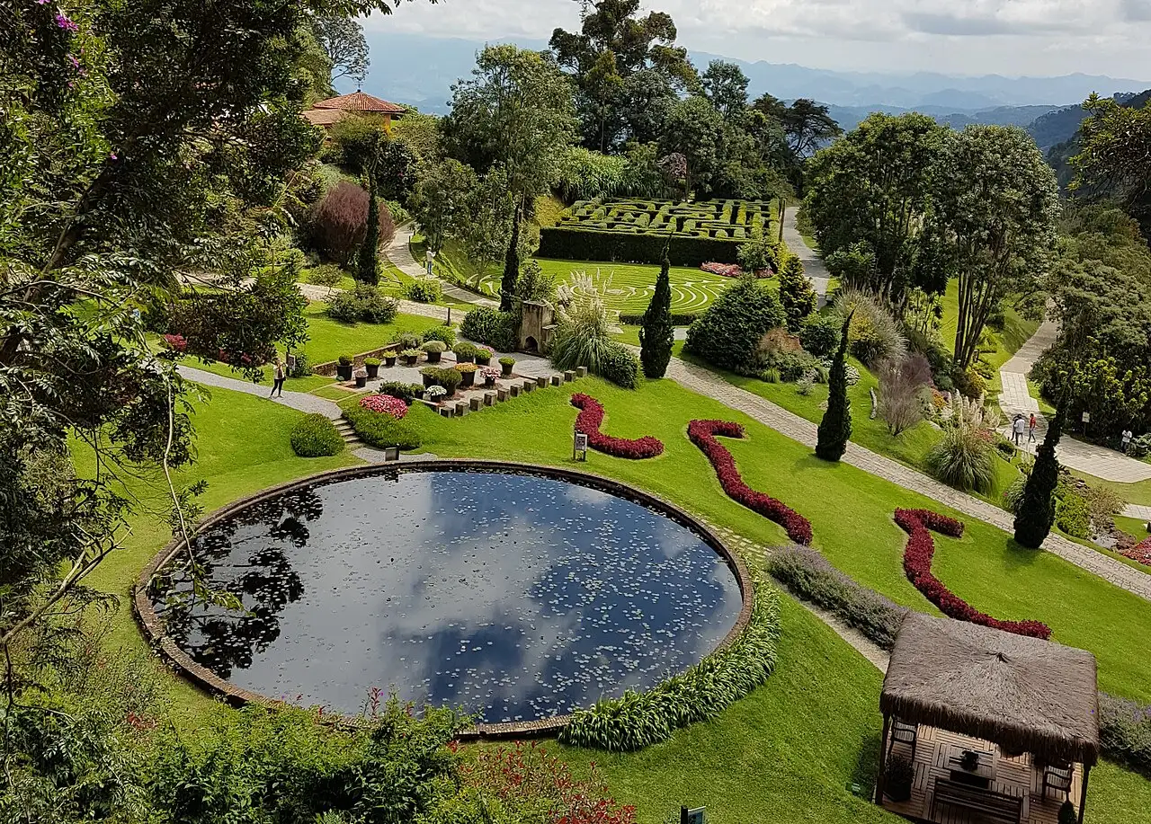 Os jardins do Parque Amantikir vistos do alto, com um lago redondo, canteiros de flores vermelhas e caminhos entre a grama.