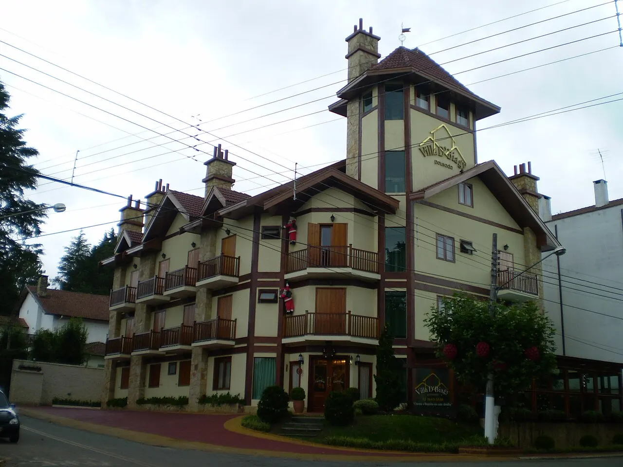 Um prédio de vários andares em estilo alpino, com telhados pontudos e torre, numa rua da Vila Capivari.