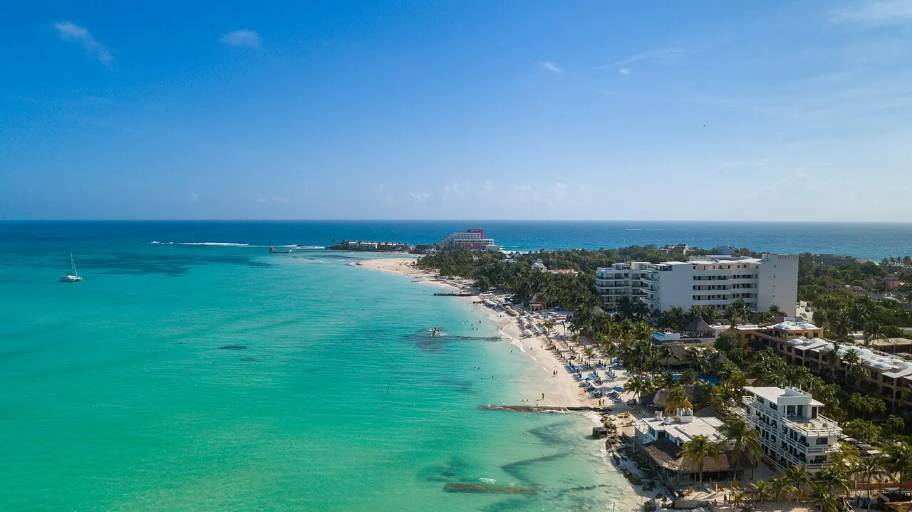 Vista aérea da Playa Norte, na ponta de Isla Mujeres, com mar turquesa muito raso, uma faixa de areia branca e hotéis baixos entre palmeiras.