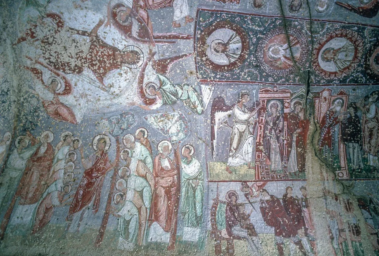 Afrescos bizantinos na parede da igreja de Nicéforo Focas, em Çavuşin, com figuras de santos em vermelho, verde e azul e medalhões, com partes desgastadas.