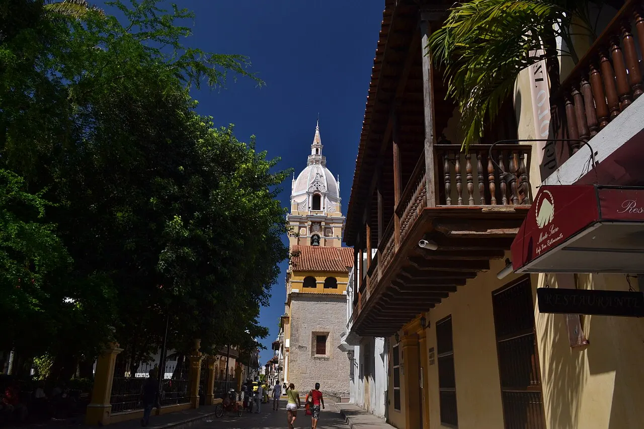 A torre da Catedral de Santa Catalina fecha uma rua de Cartagena, entre árvores e sacadas de madeira.