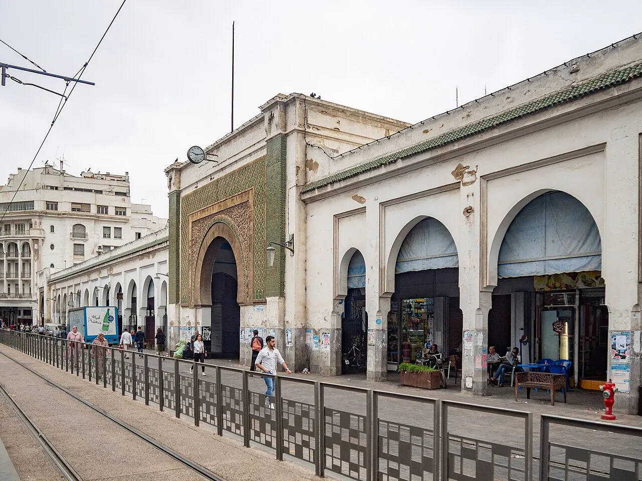 A fachada do Marché Central mostra o arco de azulejo verde, a fileira de arcadas e os trilhos do bonde na frente.