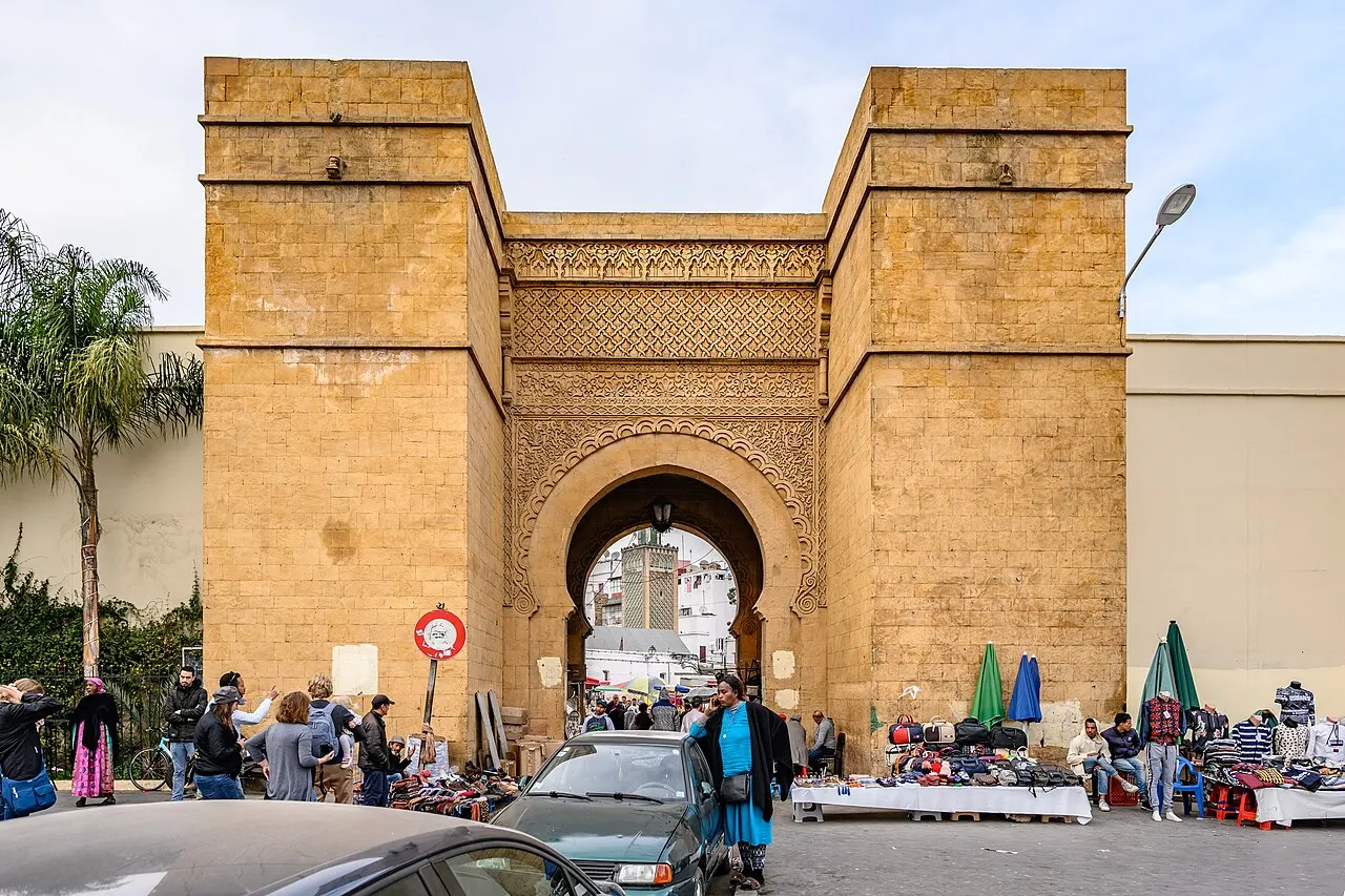 Porta em arco da muralha da medina antiga de Casablanca, entre duas torres de pedra ocre, com barracas embaixo.